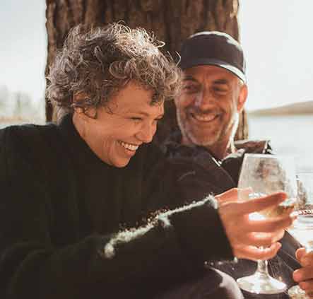 Retired couple sitting under a tree toasting with a glass of wine.