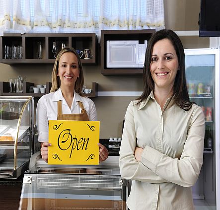 Two ladies in a shop holding an open sign image